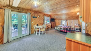 Interno di una baita con soffitto in legno, zona pranzo con tavolo e sedie, un letto con copriletto e una porta che dà su un terrazzo esterno.