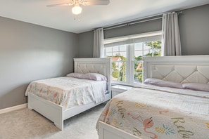 A bedroom with two beds, a ceiling fan, and a window with curtains.