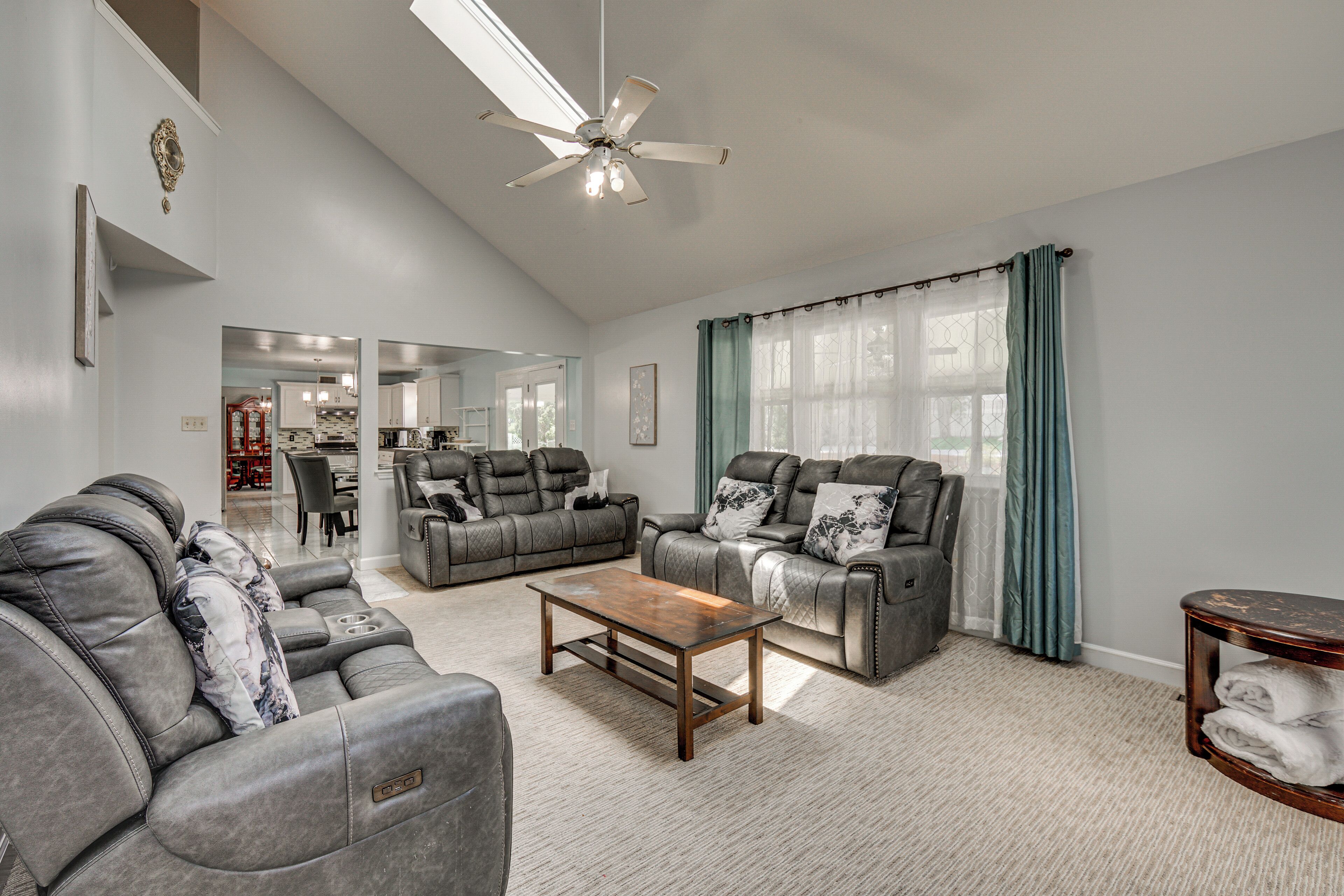 Ein geräumiges Wohnzimmer mit Deckenventilator, zwei graue Sofas mit Kissen, einem Holztisch und Blick auf den Essbereich durch ein Fenster mit Vorhängen.