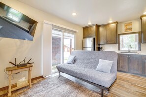 A modern kitchen with wooden cabinets, a built-in refrigerator, and a dining area with a gray sofa and a small wooden table.