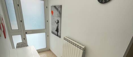 A room with a radiator, a wall clock, a table with a chair, and a window with frosted glass panels.
