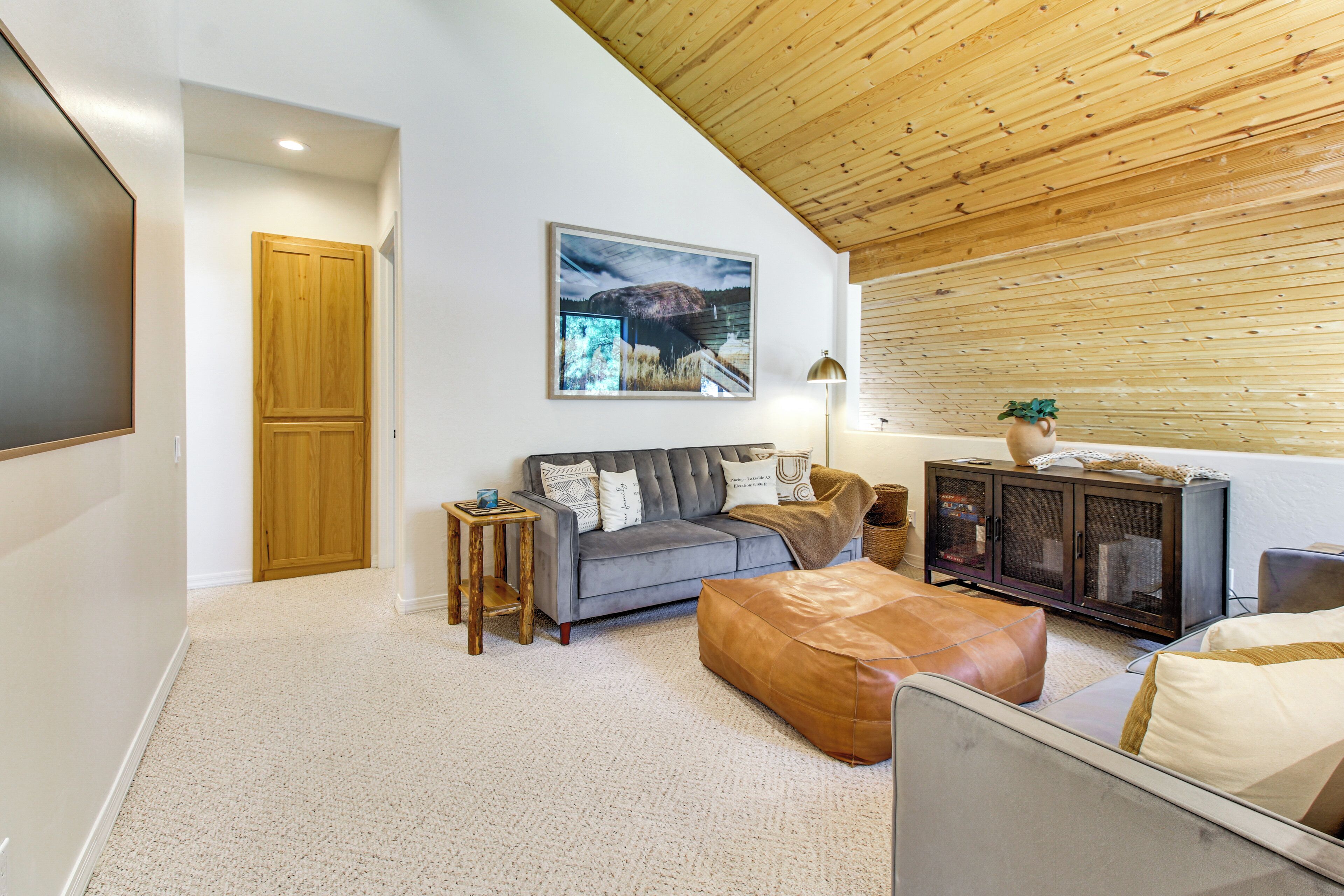 A living room with a grey sofa, a wooden cabinet, a large framed picture, and a wooden ceiling.
