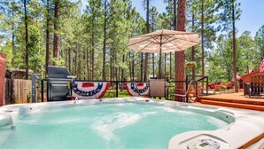 A hot tub surrounded by a wooden deck, with a flag and a grill in the background. - Deck, Fire Pit, Hot Tub! Pinetop Family Cabin (Pinetop)