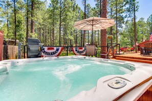A hot tub surrounded by a wooden deck, with a flag and a grill in the background. - Deck, Fire Pit, Hot Tub! Pinetop Family Cabin (Pinetop)