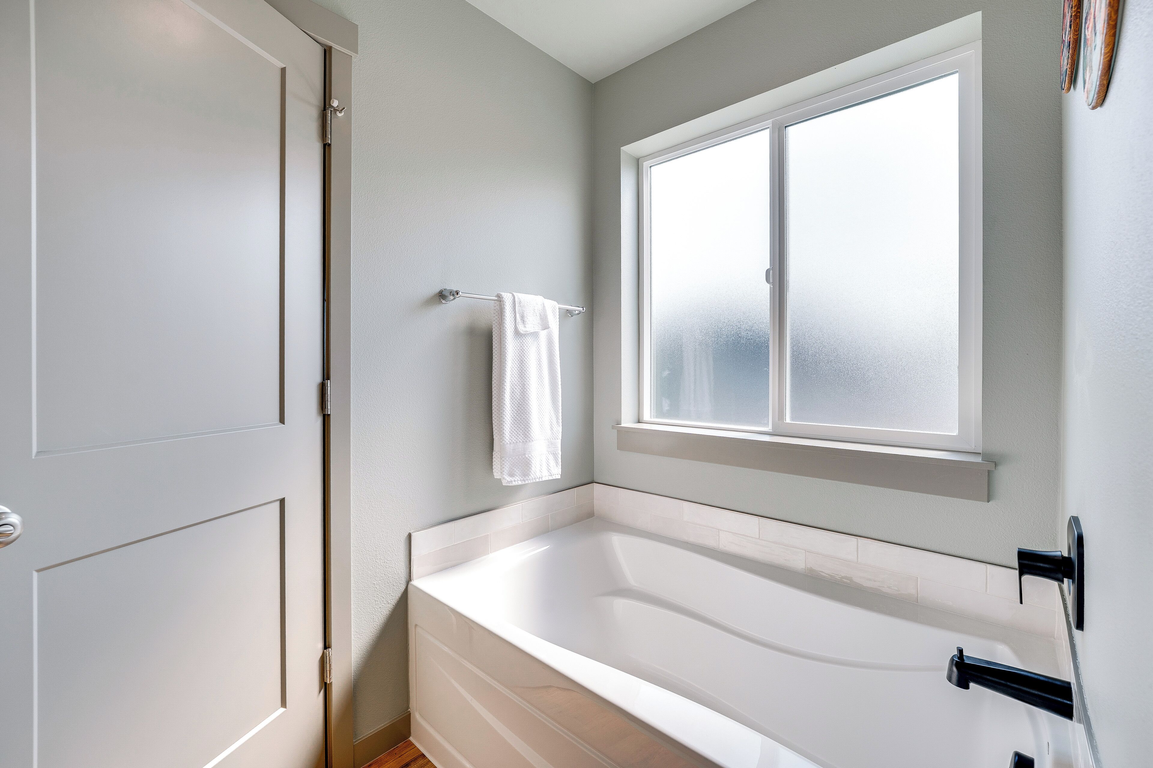 A bathroom with a bathtub, a window, and a towel hanging on a rack.