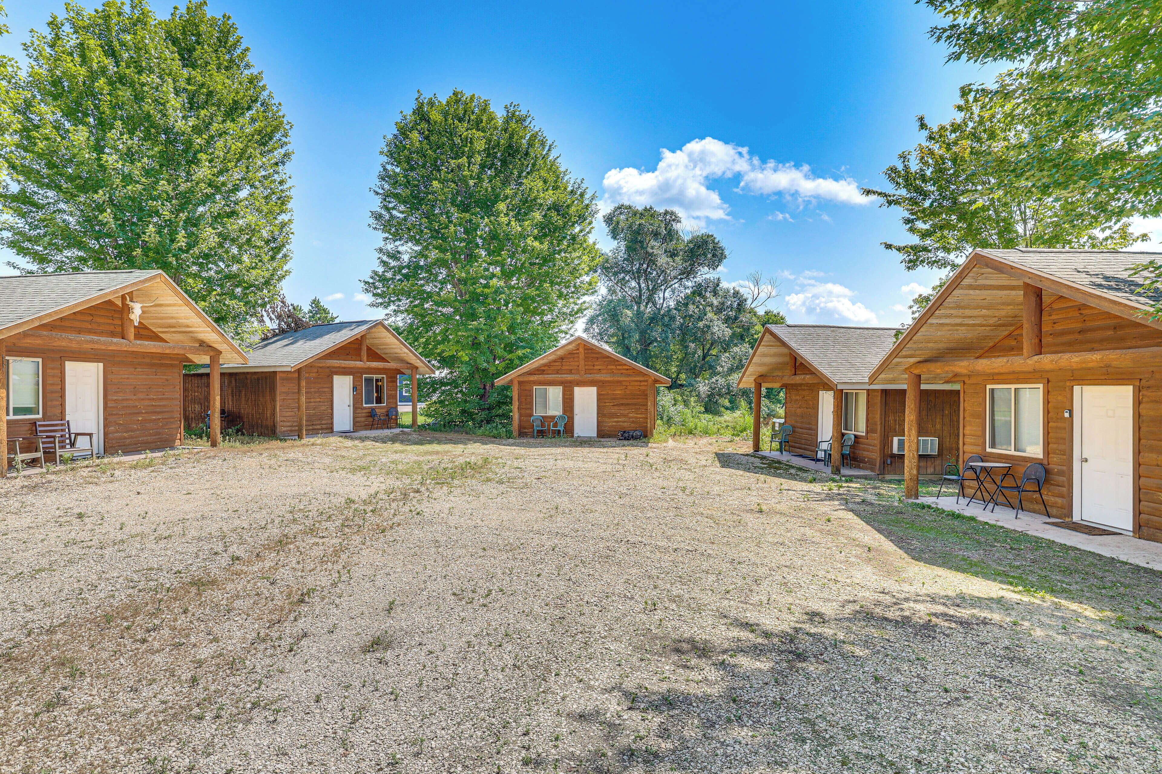A row of log cabins with a gravel driveway, surrounded by trees.