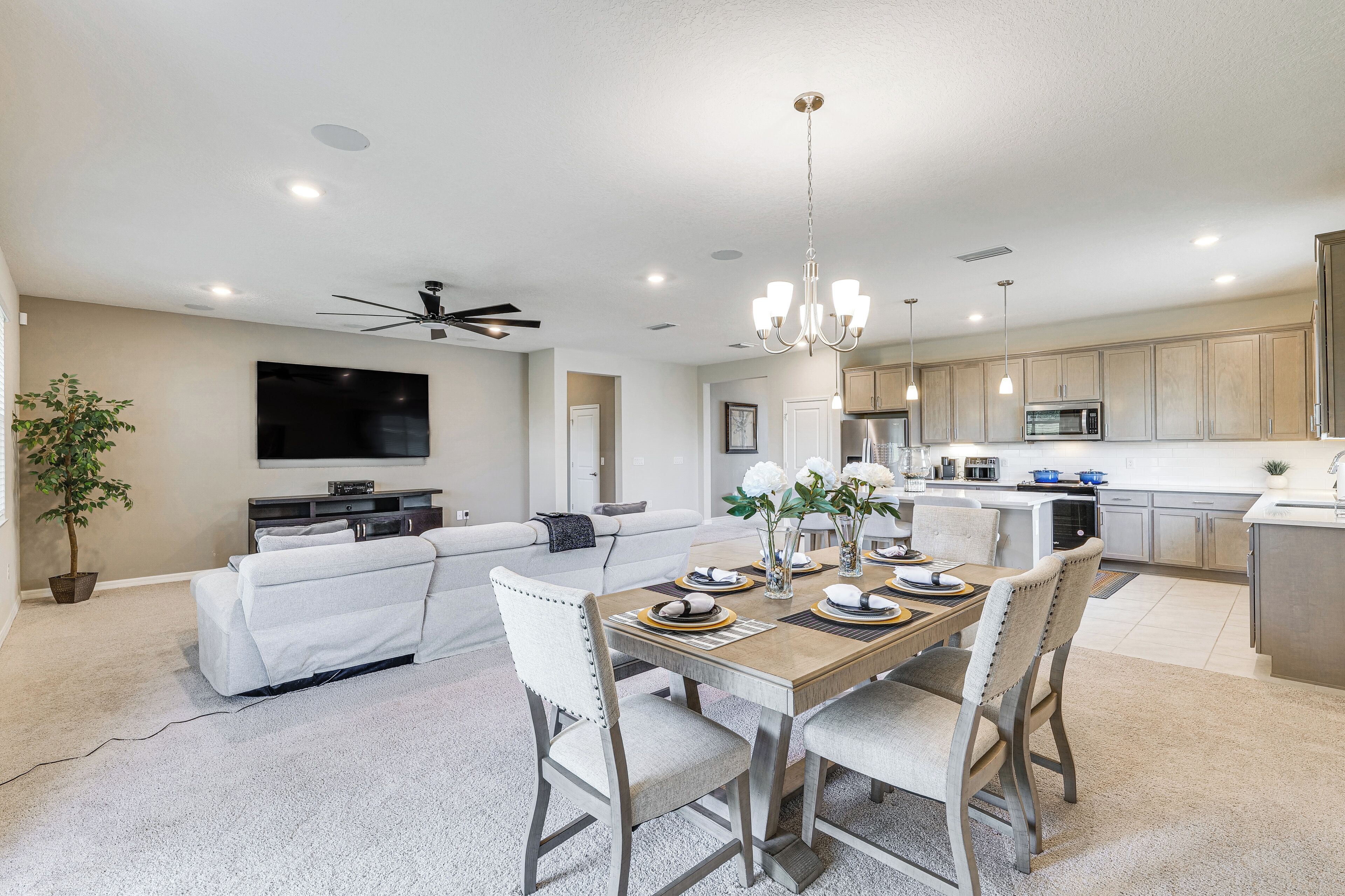 A modern living room with a flat-screen TV, a ceiling fan, and a dining area with a wooden table set for four.