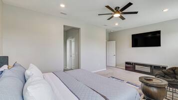 A bedroom with a bed, a ceiling fan, a flat-screen TV, and a fireplace.