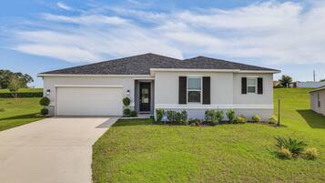 A single-story house with a garage, a front door, and a small front yard with grass and shrubs.