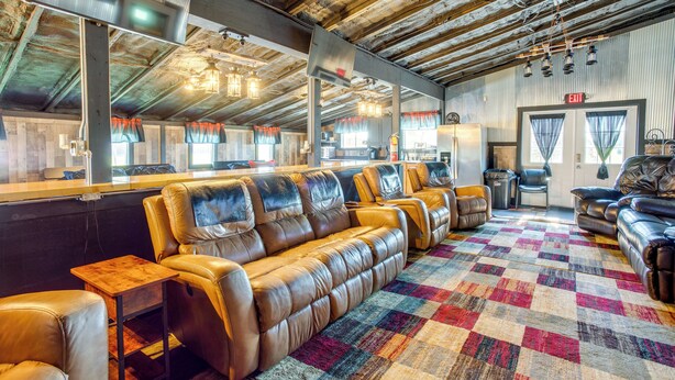 A spacious lounge area with leather seating, a patterned rug, and a high ceiling with exposed beams. - Cast & Relax! Lake-view Fishing Cabin in Monmouth (Monmouth)