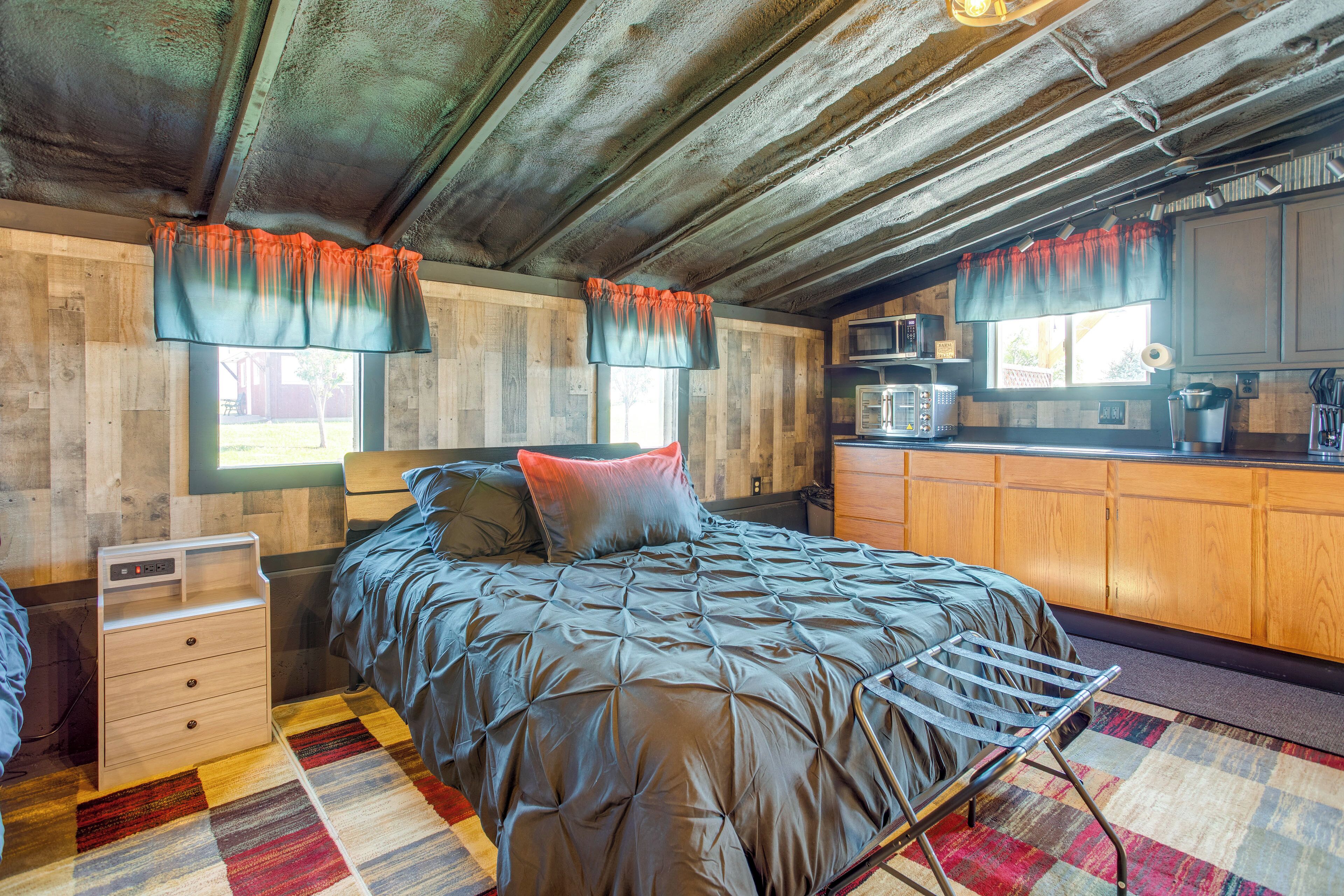 A bedroom with a bed, a wooden wardrobe, a small desk, and a kitchenette.