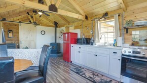 A cabin interior with a wooden ceiling, a dining area with a table and chairs, a kitchen with appliances, and a large window.