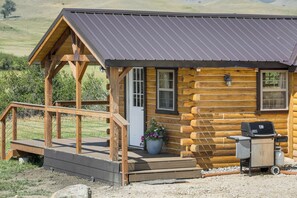 A log cabin with a porch, a grill, and a view of the surrounding landscape.