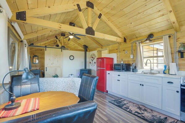 A cozy cabin interior with a wooden ceiling, a dining area with a table and chairs, a kitchen with white cabinets, and a red refrigerator.