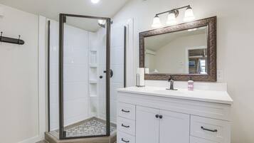 A bathroom with a glass-enclosed shower, a white vanity with a mirror, and a tiled floor.
