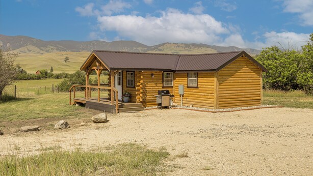 A wooden cabin with a porch, a small deck, and a gravel driveway.
