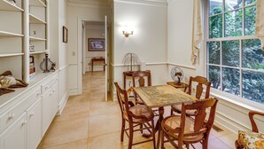 Un comedor con una mesa, sillas, una araña y vistas a follaje a través de una ventana.