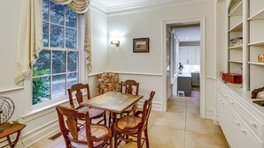 Un comedor con una mesa y sillas, una ventana con cortinas, una lámpara de pared y una puerta que da a una cocina.