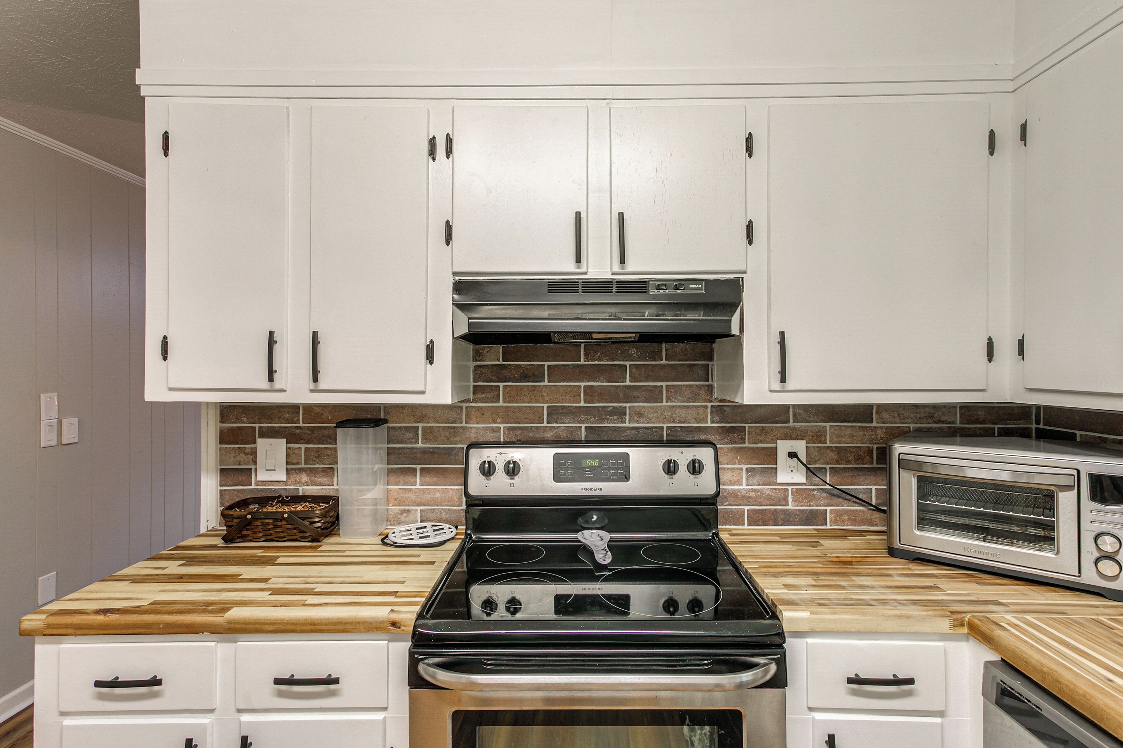 A kitchen with white cabinets, a stainless steel stove, a toaster, and a brick backsplash.