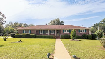 A two-story brick house with a front lawn, a pathway leading to the front door, and a small garden area.