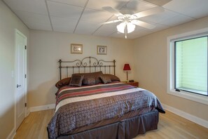 A bedroom with a bed, a ceiling fan, a window with blinds, and a nightstand with a lamp.