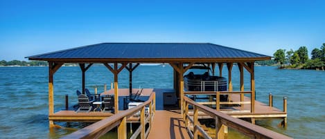 A wooden dock leading to a covered seating area with chairs and a table, overlooking a body of water.