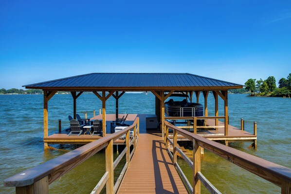 A wooden dock leading to a covered seating area with chairs and a table, overlooking a body of water.