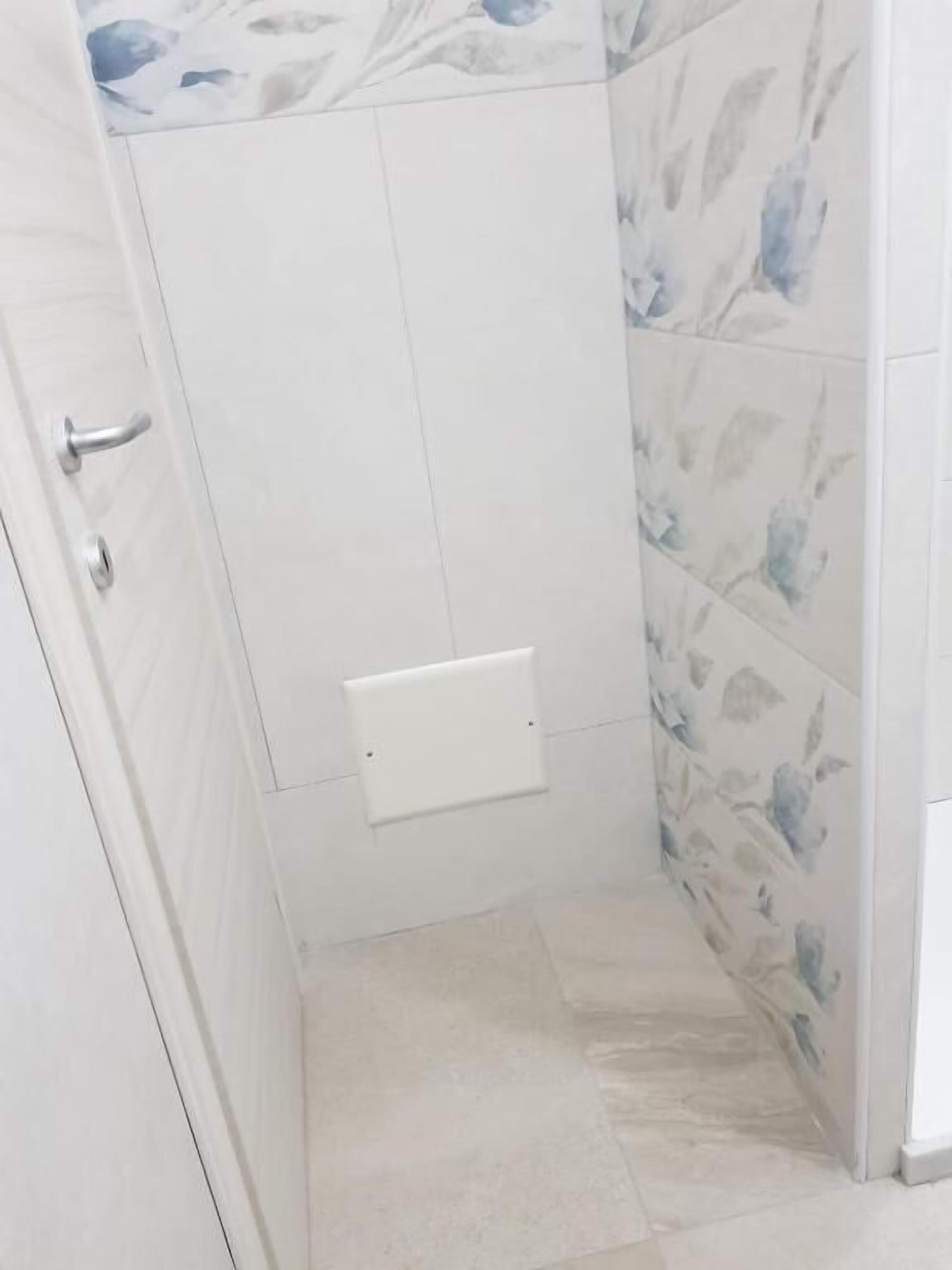 A narrow bathroom with white tiles and a floral pattern on the walls.