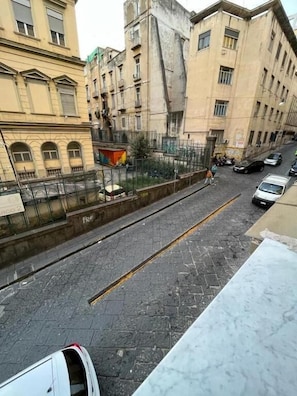 Straßenansicht mit Gebäuden, einem Zaun und parkenden Autos.