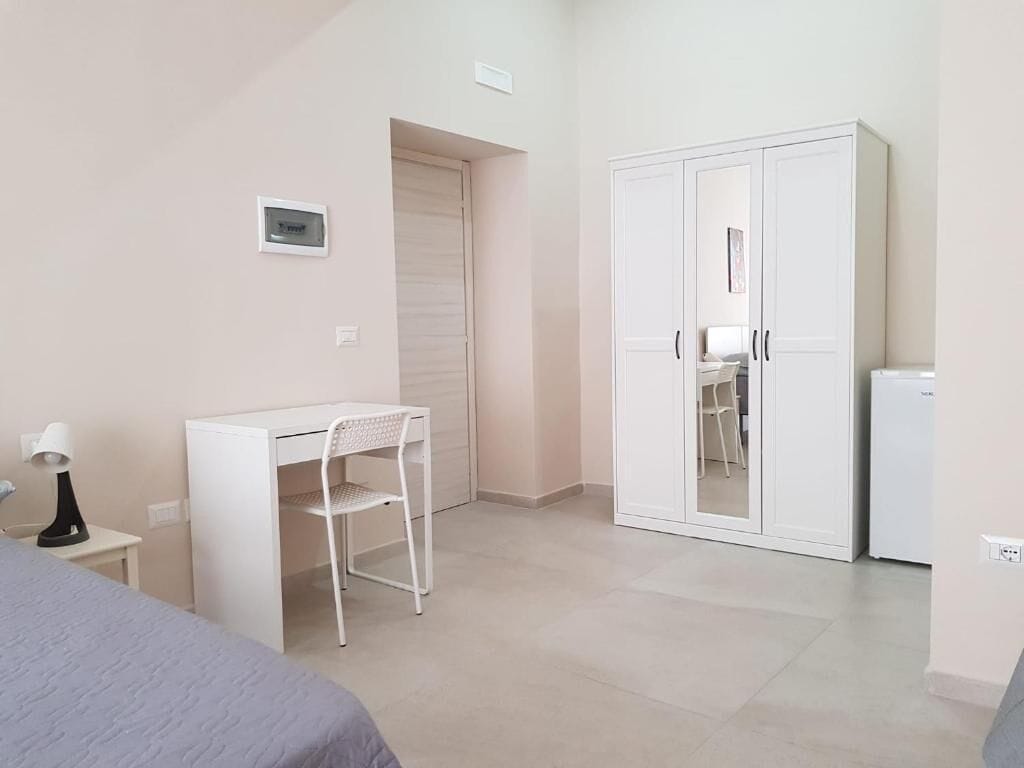 A bedroom with a bed, a desk, a chair, a wardrobe, and a small table.