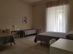 Quarto de hotel com duas camas, uma escrivaninha, uma cadeira e uma janela com cortinas.