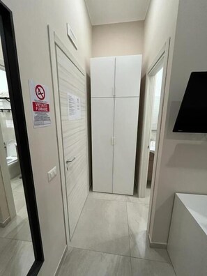 Un pasillo estrecho con un armario, una puerta con el letrero de prohibido fumar y una lámpara fijada a la pared.