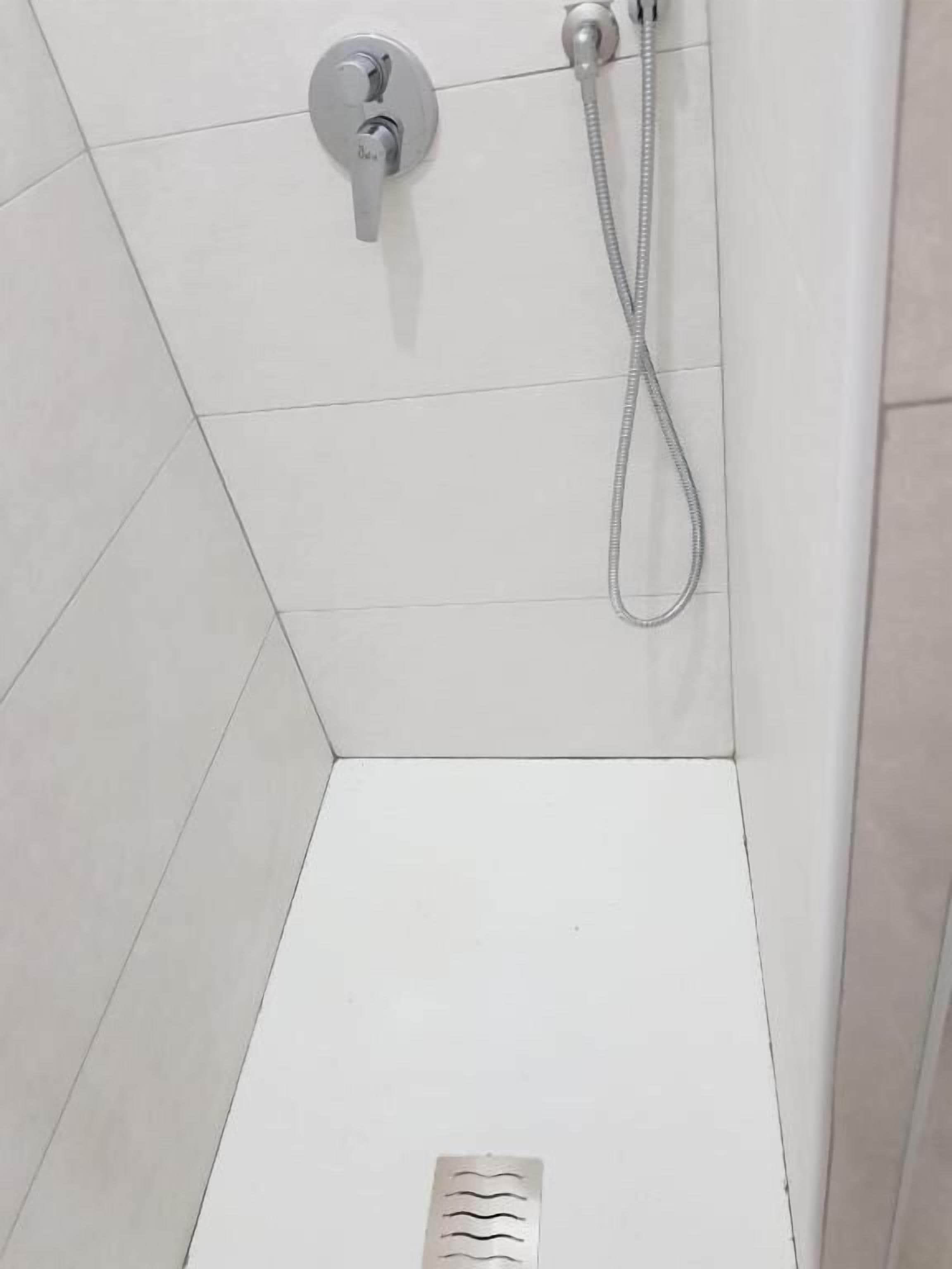 Un espacio de ducha con un cabezal de ducha de mano y un grifo empotrado.