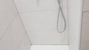 Un espacio de ducha con un cabezal de ducha de mano y un grifo empotrado.