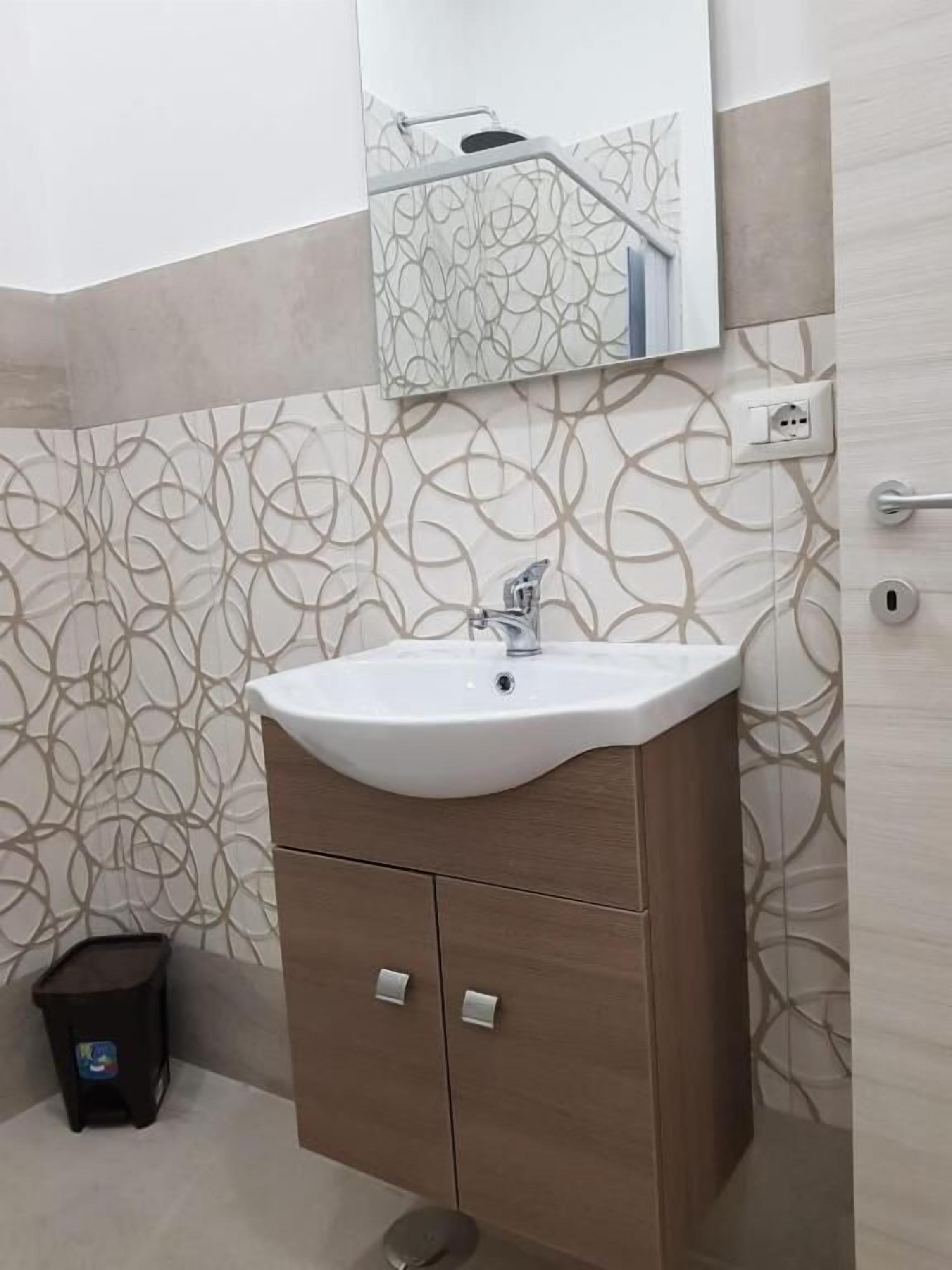 A bathroom with a white sink, wooden cabinet, and patterned wall tiles.