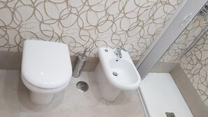 Een badkamer met toilet, bidet en een klein kastje.