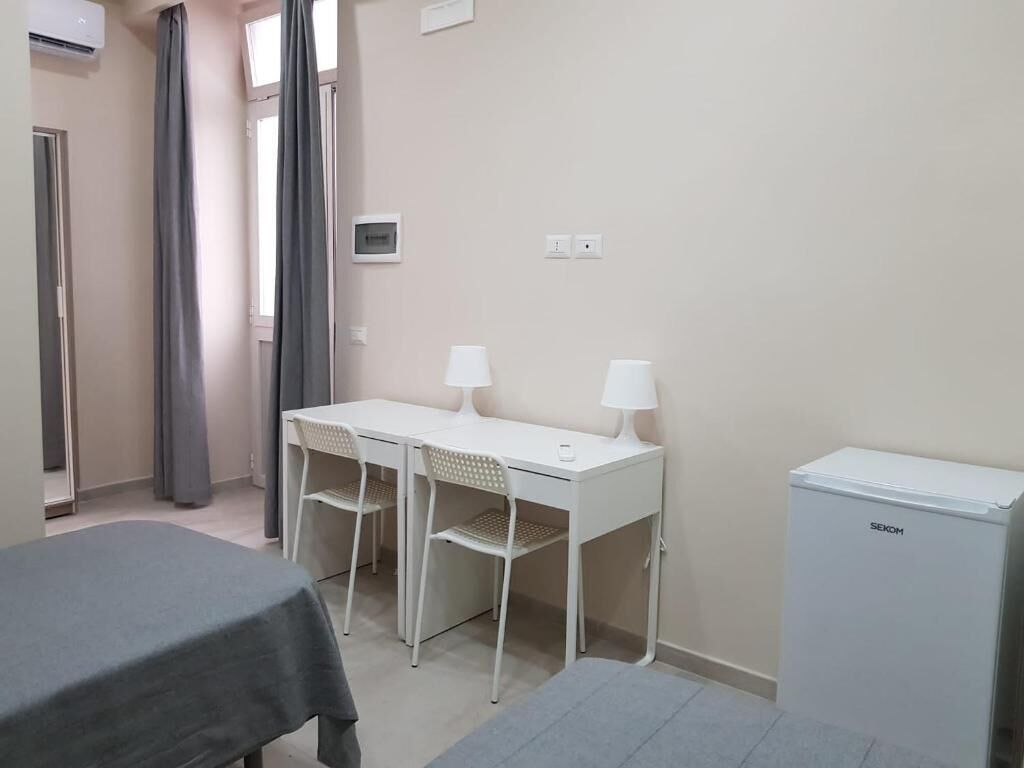 Une chambre d’hôtel comprenant un lit, un bureau avec deux chaises, un petit réfrigérateur et une fenêtre avec des rideaux.