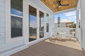 Eine überdachte Terrasse mit weißen Geländern und Stühlen, einem Deckenventilator und Blick auf den Garten.