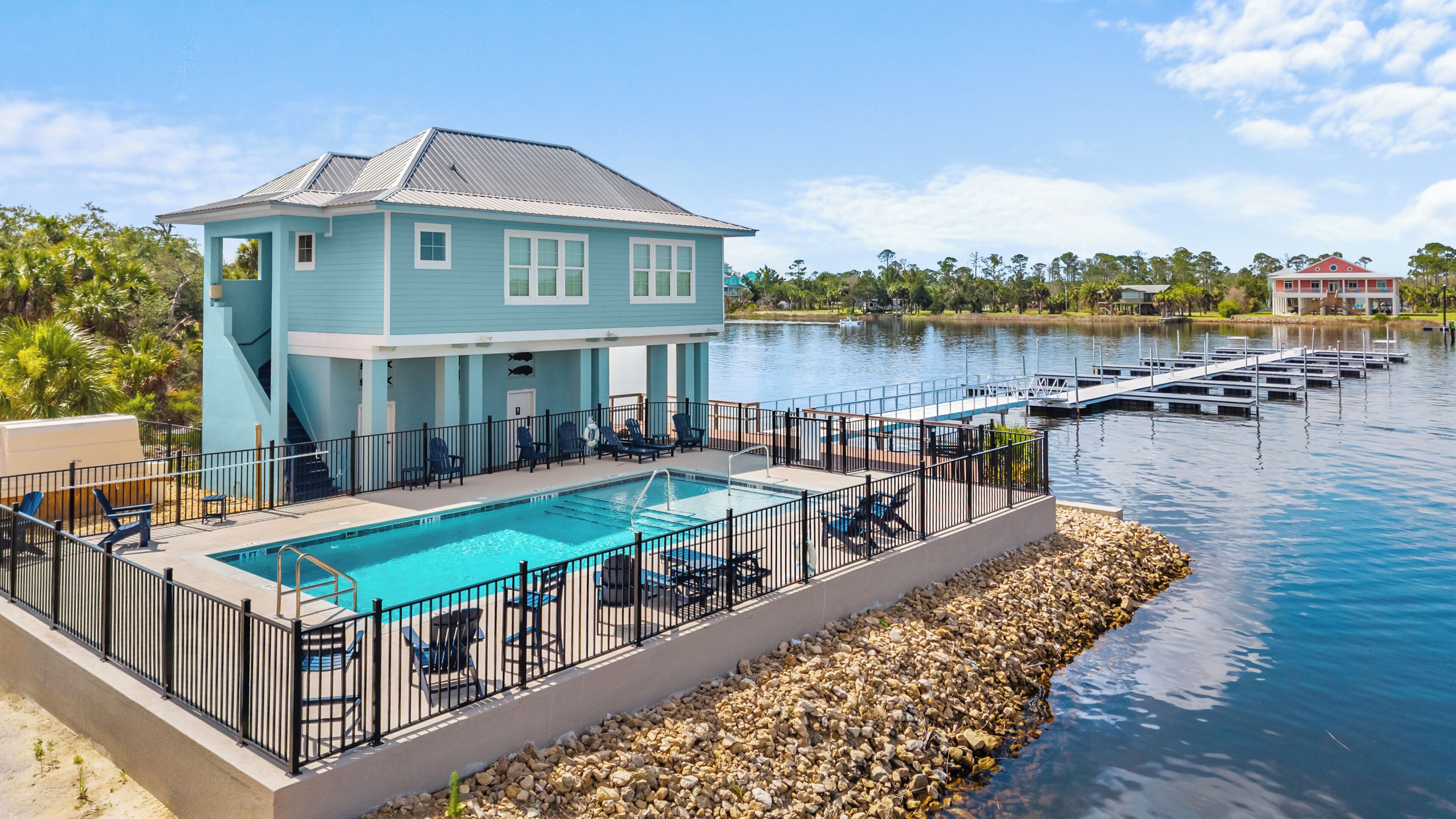 A light blue building with a pool and dock, surrounded by water and greenery.