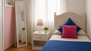 Ein Schlafzimmer mit einem Bett, einem Nachttisch mit Lampe, einem Spiegel und einem Fenster mit Vorhängen.