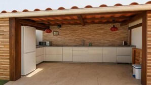 Eine Küche mit Fliesenboden, Holzschränken, einem Kühlschrank, einer Mikrowelle und einem Spülbecken.
