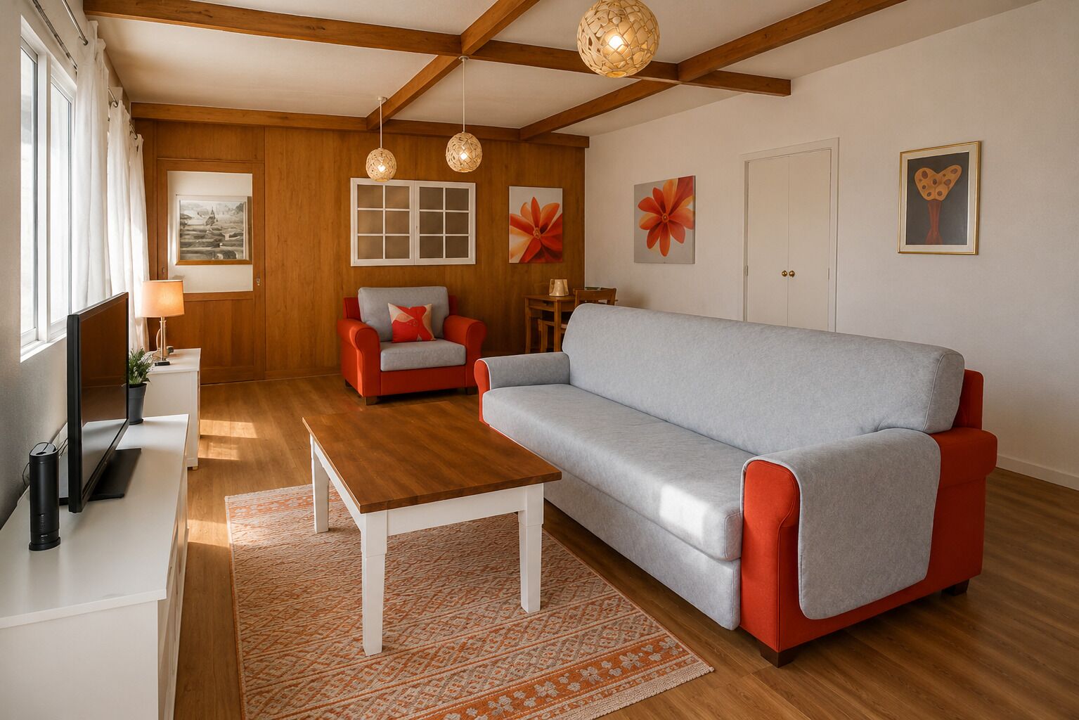 Een moderne woonkamer met een grijze bank, rode fauteuils, houten vloeren en een televisie.