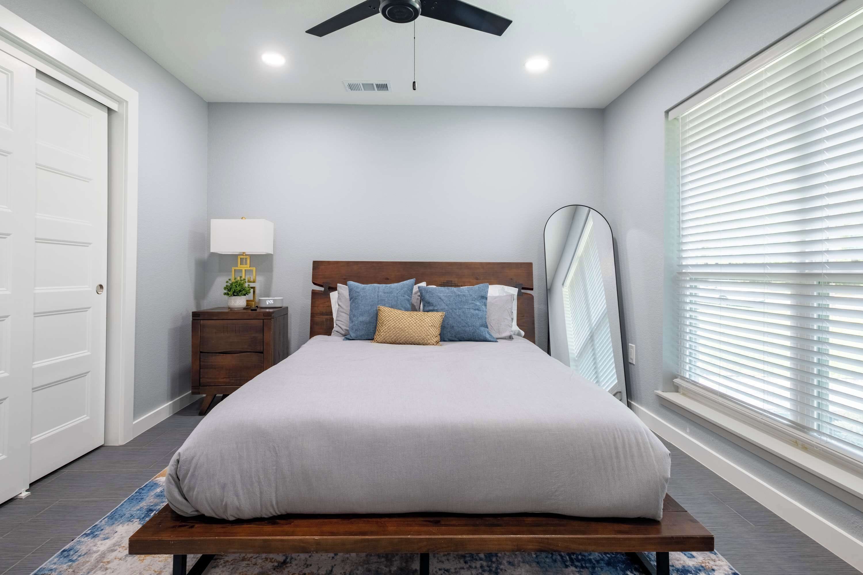 A bedroom with a bed, bedside table, lamp, and a ceiling fan.