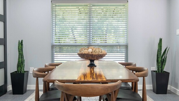 A dining area with a rectangular table, six chairs, a central woven basket, and two potted plants. - Bright Dallas Retreat with Fire Pit & Games (Dallas)