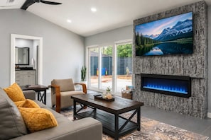 A modern living room with a fireplace, a television mounted on a textured wall, and a view of a mountain landscape. - Bright Dallas Retreat with Fire Pit & Games (Dallas)