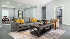 A modern living room with a grey sofa, a coffee table, and a ceiling fan. - Bright Dallas Retreat with Fire Pit & Games (Dallas)