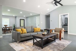 A modern living room with a grey sofa, a coffee table, and a ceiling fan. - Bright Dallas Retreat with Fire Pit & Games (Dallas)