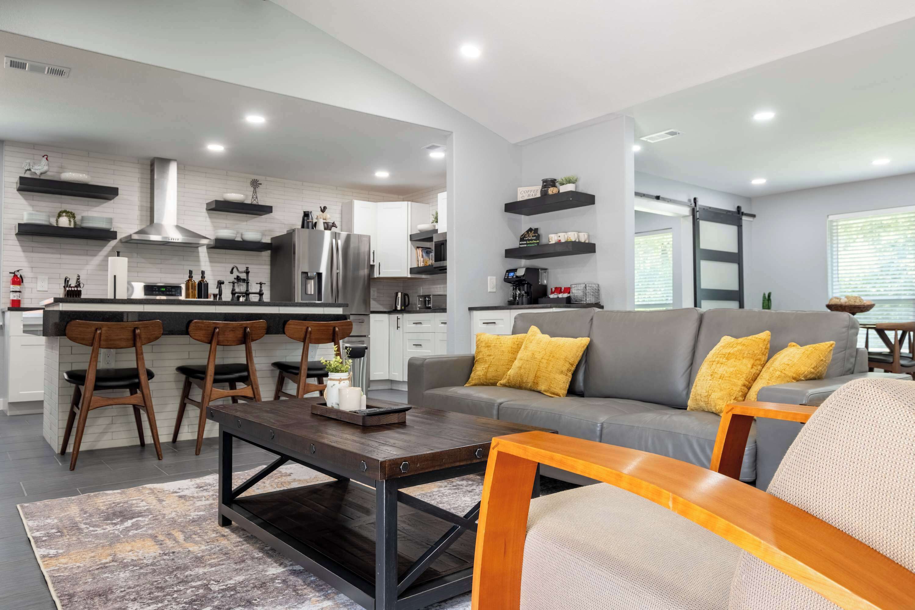 Una cocina moderna con una isla central, taburetes de bar y una zona de comedor con un sofá y una mesa de centro.