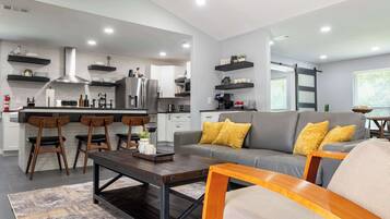 Una cocina moderna con una isla central, taburetes de bar y una zona de comedor con un sofá y una mesa de centro.