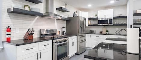 A modern kitchen with white cabinetry, stainless steel appliances, and black countertops.